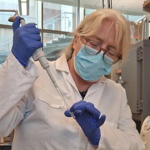 Micaela står i labbet med en vit rock och blåa handskar. Hon jobbar på ett eDNA projekt.